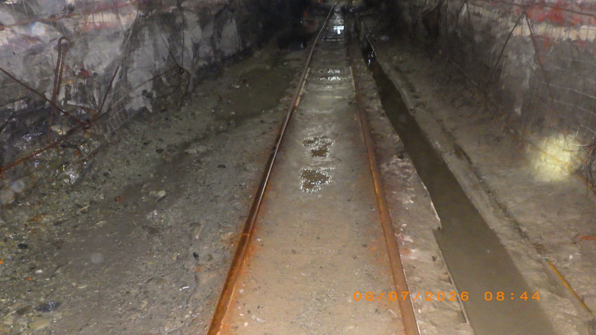 Cross Cut Management: Concreted track and drain. Concrete footwall poured between and along the rails, with a formed concrete drain along the sidewall.