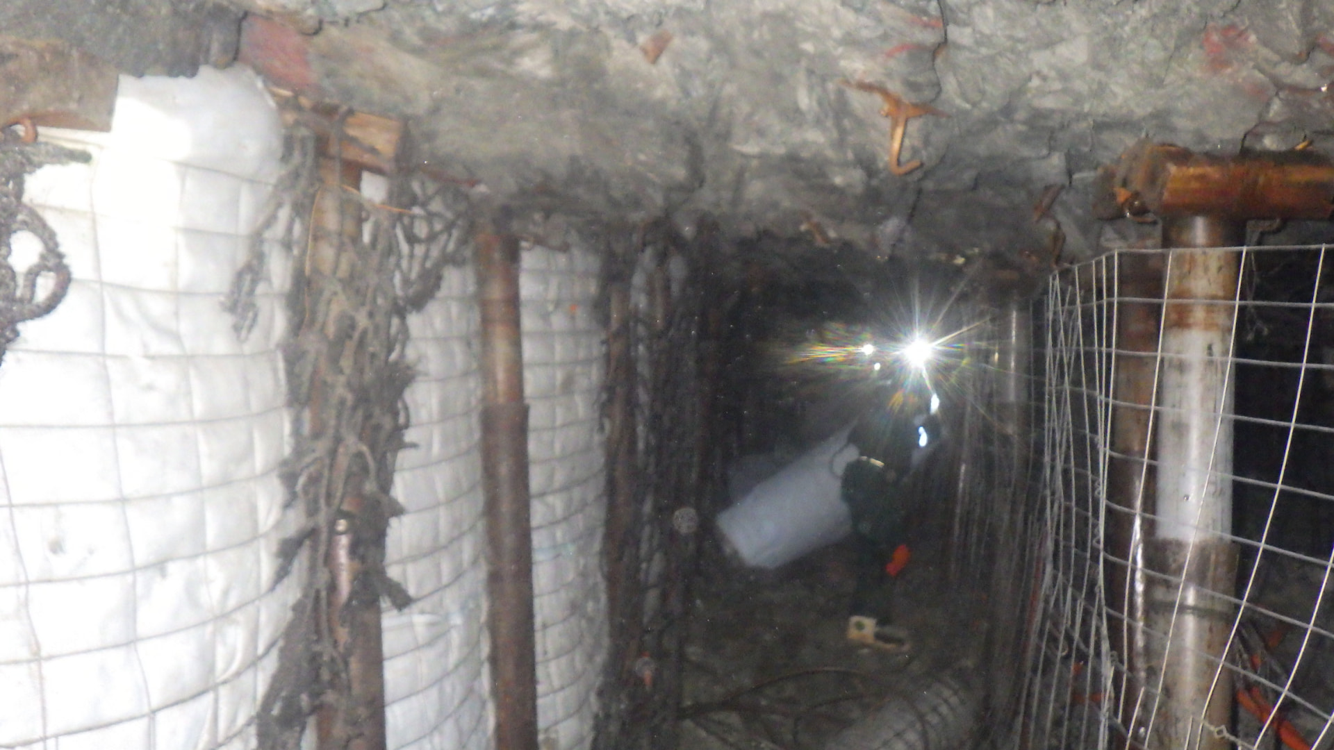 Backfill Contracting: Crew preparing the backfill line. A crew member handling backfill fabric in the stope passage, with bagged backfill on one side and a mesh-and-prop line on the other.