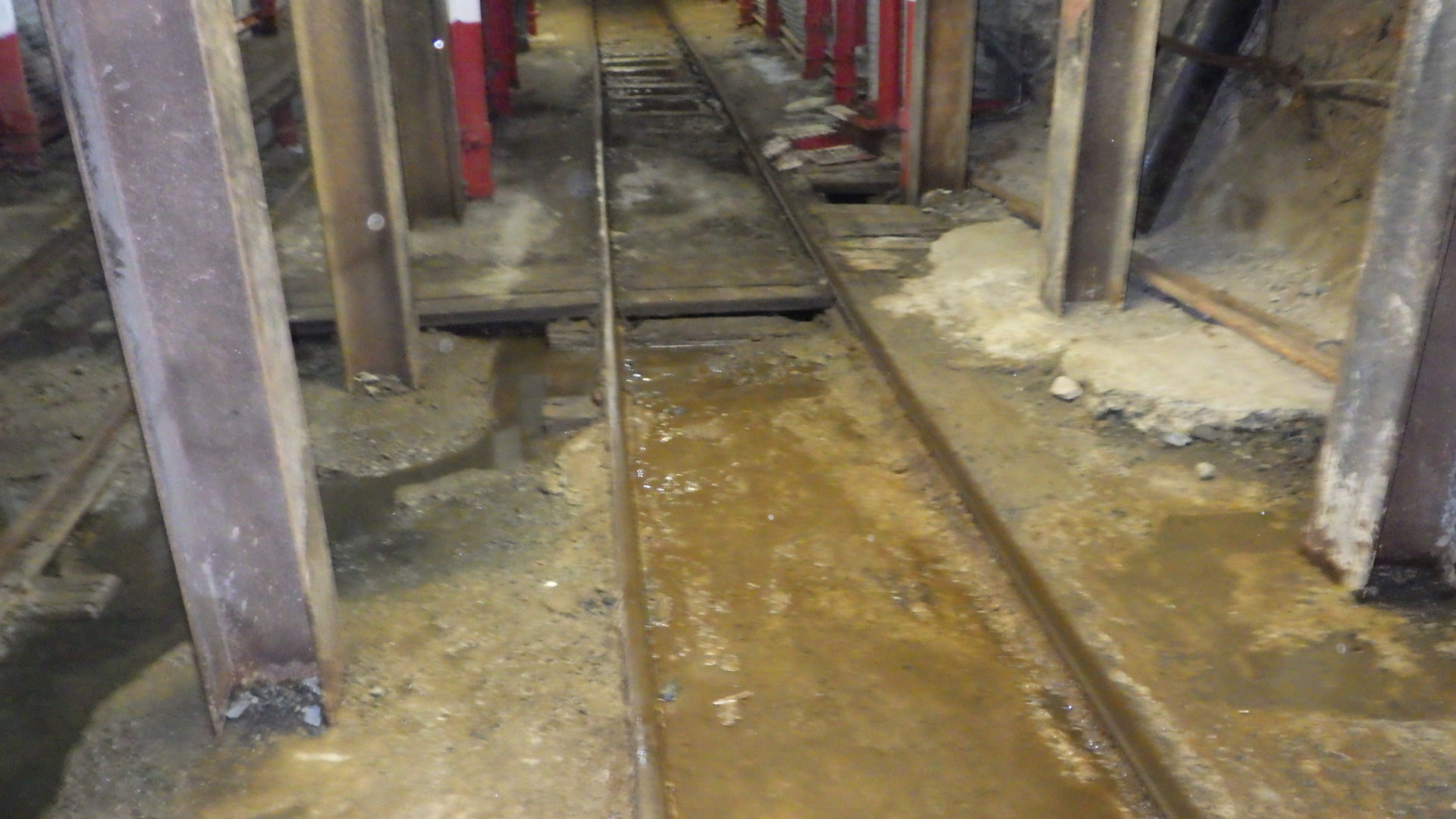 Cross Cut Management: Flooded crosscut. Standing water and thick slurry covering the rails and ballast, creating derailment and slip hazards before cleanup.